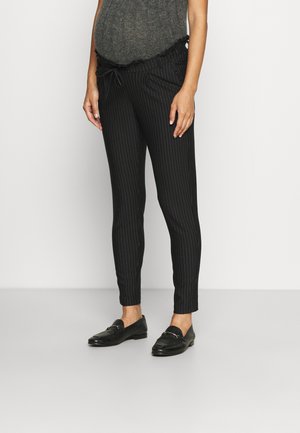 Pantalons noirs à rayures, avec une taille à cordon de serrage, comportant des poches et un design ajusté. Associés à des mocassins noirs.