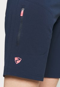 Námořnické modré sportovní šortky s kapsou na zip a růžovým táhlem a růžovým logem na dolní části nohavic. Hladká textura.