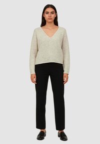 Maglione a maglia beige chiaro con scollo a V e maniche lunghe, abbinato a pantaloni neri a gamba dritta e mocassini neri. Tessuto liscio con piccole sfumature.