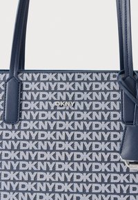 Granatowa torba typu tote z wzorem logo DKNY w kolorze białym, wykonana z teksturowanej tkaniny z akcentami ze skóry i solidnymi uchwytami.
