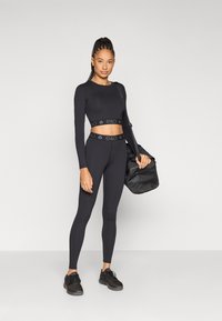 Μαύρο αθλητικό σετ δύο τεμαχίων που περιλαμβάνει ένα κοντό μακρυμάνικο τοπ και κολάν ψηλού καβαλού με λωρίδες λογότυπου. Λείο φινίρισμα, σε συνδυασμό με μια σκούρα τσάντα.