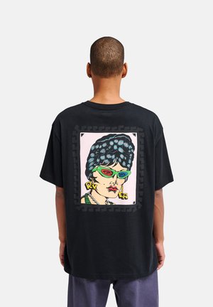 Persona che indossa una maglietta nera con un ritratto pop art colorato di una donna con occhiali 3D verdi e trucco audace sulla schiena.