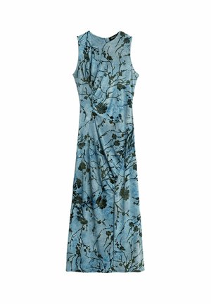 Woman with braided hair wearing a sleeveless, light blue maxi dress with black floral patterns, standing with one hand on her hip and black heels.