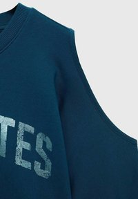 Turkizna pa sweatshirt z dizajnom širokih ramen, rebrastim izrezom in teksturiranim grafičnim besedilom v srebrni barvi. Mehka, gladka tkanina z minimalnim šivanjem.