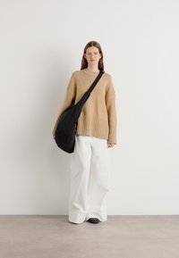 Beige geribbelde trui, witte wijde broek en een zwarte schoudertas. Gladde texturen, relaxte pasvorm, neutraal kleurenpalet. Eenvoudig ontwerp.