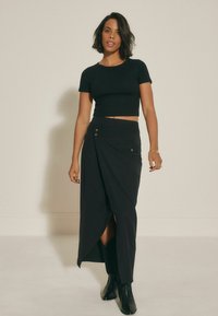 Tricou scurt negru cu mâneci scurte, asociat cu o fustă lungă, asimetrică, neagră, ce prezintă două nasturi decorative și o fanta laterală.