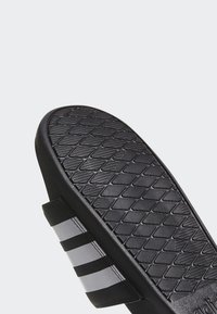 Sandal di gomma nera con suola testurizzata, caratterizzato da tre strisce bianche sulla parte superiore. Il design è minimalista e sportivo.