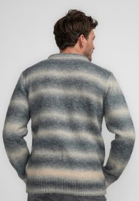Suéter de punto con un diseño a rayas en tonos de gris y crema, tejido texturizado, y un cuello y dobladillo acanalados.