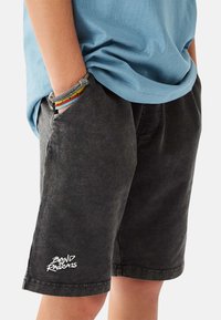 Musta farkkushortsit kuluneella tekstuurilla, joissa on sivutaskut ja valkoinen "BAND OF RASCALS" -logo helmassa.