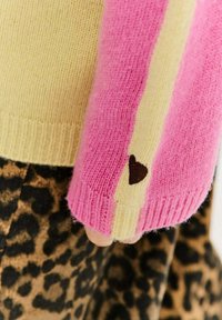 Pletený sveter v ružových a krémových farbách, s rebrovanými manžetami a srdiečkovým detailom. Spárovaný s čiernobielou sukňou s leopardím vzorom.