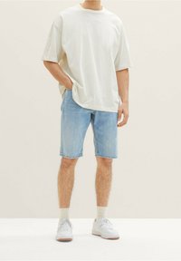 Camiseta de algodón de gran tamaño en gris claro combinada con pantalones cortos de mezclilla azul claro. Zapatillas blancas y calcetines crema completan el conjunto casual.