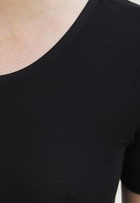 Schwarzes, enganliegendes T-Shirt mit rundem Halsausschnitt und kurzen Ärmeln. Hergestellt aus glattem, dehnbaren Stoff mit einer subtilen Textur.
