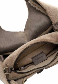 Sac à main en cuir marron avec une doublure en tan douce et texturée. Dispose d'une poche zippée, d'une étiquette intérieure et d'un design d'ouverture incurvée.