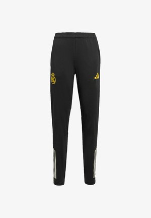 Mustat urheiluhousut, joissa on keltainen Real Madridin logo ja Adidaksen brändäys. Varustettu valkoisilla sivuraidoilla ja joustavalla vyötäröllä mukavuutta varten.