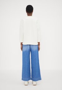 Vit sweatshirt med sänkta axlar, kombinerad med vida blå denimjeans som har en blekt fåll. Skorna är vita med rundade tår.