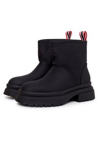 Botas negras de tobillo con acabado mate, suela de goma gruesa y tiradores de rayas rojas y blancas en la parte superior para facilitar su uso.