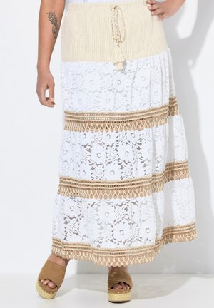 Jupe maxi en dentelle blanche avec une ceinture en tricot beige, ornée de motifs complexes et d'accents tressés, associée à des sandales à plateforme marron.