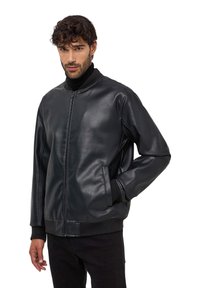 Czarna skórzana kurtka bomberka o gładkiej fakturze, z prążkowanymi mankietami i zapięciem na zamek. Posiada boczne kieszenie. Noszona na czarnym golfie.