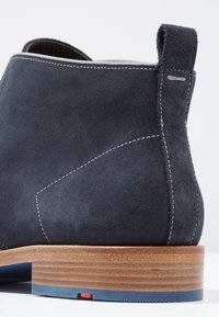 Bottines en daim noir marine, avec des coutures contrastantes, un talon en bois avec des accents bleu et rouge, et un bout rond.