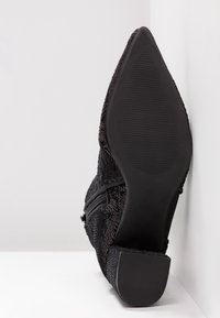 Scarpa nera con tacco alto, con tomaia in tessuto texture e suola in gomma. Design a basso taglio con punta affilata e chiusura con zip laterale.