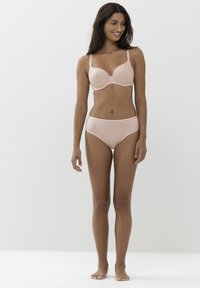 Jasno nude stanik i dopasowane wysokie figi, gładki materiał, wsparcie z fiszbinami oraz bezszwowy fason z minimalnymi detalami.