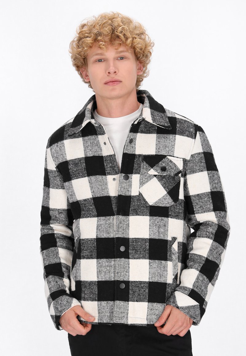 Mustriline mustvalge jakki valmistatud tekstureeritud kangast, millel on krae, nõtkuvad nööbid ja rinnaesine tasku klapiga.