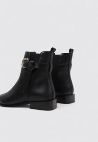 Black leather ankle boots with a matte finish, featuring a gold-tone buckle accent and low block heels. Simple and sleek design.