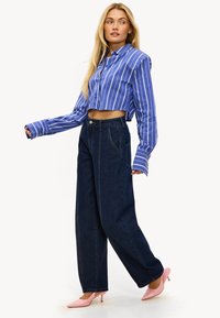 Camisa azul a rayas recortada con mangas largas, combinada con pantalones sueltos de mezclilla oscura de talle alto y tacones rosas brillantes.