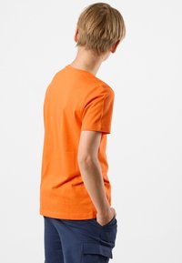 Orange bomulds T-shirt med korte ærmer, rund halsudskæring og en afslappet pasform, båret med mørkeblå cargo shorts. Vist fra bagsiden.