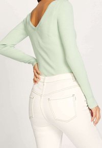 Minzgrünes, geripptes Langarmshirt mit tiefem V-förmigem Rückenausschnitt, kombiniert mit hoch taillierten weißen Jeans mit kontrastfarbigen Nähten und Gesäßtaschen.