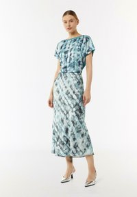 Turkusowa bluzka w stylu tie-dye z krótkim rękawem, połączona z dopasowaną spódnicą o średniej długości, która ma podobny wzór i gładką teksturę.