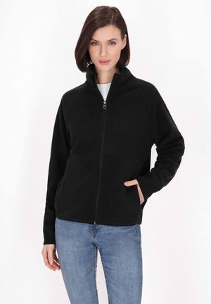 Jachetă neagră din fleece cu guler înalt, fermoar frontal și două buzunare laterale. Are mâneci raglan și o textură netedă. Este asociată cu blugi albaștri.