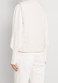 Biała pikowana kamizelka z teksturowanym plecami z dzianiny, prążkowanym dołem i długimi balonowymi rękawami, prezentująca minimalistyczny design i miękki materiał.