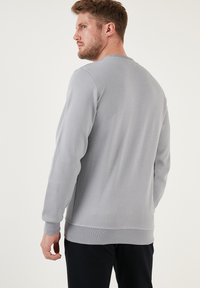 Felpa grigia a maniche lunghe realizzata in tessuto testurizzato, con scollo rotondo e polsini a costine. Presenta una vestibilità regolare e un design minimalista.