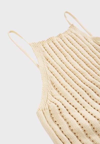 Haut beige en maille sans manches avec fines bretelles et motif côtelé vertical sur un fond clair.