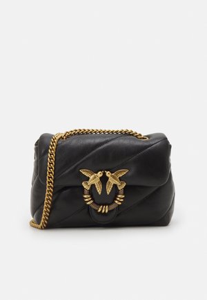 Sac à main en cuir noir avec un design matelassé, une bandoulière chaîne dorée et une fermeture décorative ornée de deux oiseaux. Texture lisse avec des accents audacieux.