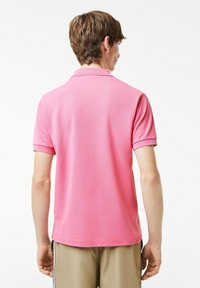 Rosa polo-tröja med krage, korta ärmar och textilstruktur. Har rak nederkant och ribbade ärmslut.