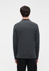 Πόλο μπλούζα με μακριά μανίκια σε σκούρο γκρι ύφασμα. Διαθέτει γιακά και ίσιο τελείωμα. Το υλικό φαίνεται λείο με ελάχιστη υφή.