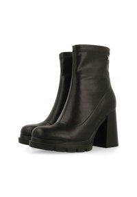 Botines de cuero negro hasta el tobillo con un alto tacón cuadrado, que presentan un acabado suave, punta redondeada y un diseño minimalista.