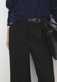 Zwarte op maat gemaakte broek met een relaxed fit, gecombineerd met een marineblauw sweater en een zwarte leren handtas met een gouden accent.