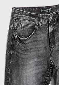 Črne denim hlače z ožganim finišem, s klasičnim pet-pocket dizajnom, kovinsko strojno opremo in oznako, ki prikazuje velikost 38.