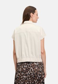 Jasno beżowa kurtka na krótki rękaw z dopasowaną talią i detalem w okolicy pleców, zestawiona z plisowaną spódnicą w leopardzi wzór.