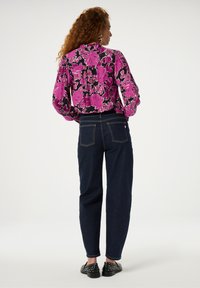 Floral blouse with puff sleeves in pink and black, paired with dark denim jeans. Blouse features a high collar and relaxed fit.