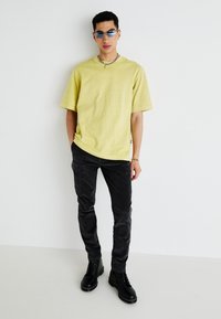 Žlté oversized tričko, čierne slim-fit nohavice a čierne šnurovacie členkové čižmy. Poznámka: detaily modro zafarbených slnečných okuliarov a reťazového náhrdelníka.