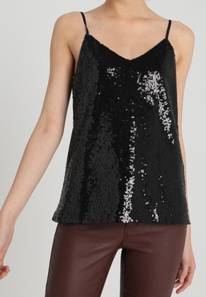 Woman wearing a black sequin spaghetti strap top paired with brown leather pants, shown from shoulders to hips.