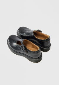 Μαύρα παπούτσια slip-on με υφή κροκοδείλου, λουρί στην πλάτη και κίτρινη λεπτομέρεια. Διαθέτουν άνετο εσωτερικό και παχύ ελαστικό πέλμα.