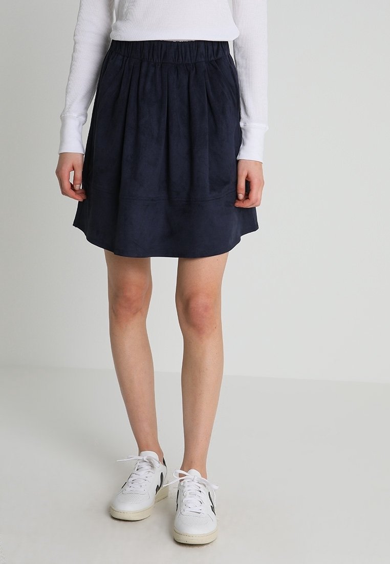 Gonna in suede blu navy con vita elastica arricciata, forma ad A e texture liscia. Indossata con sneakers bianche.