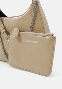 Beige värinen patenttinen nahkalaukku ketjuhihnalla, jossa irrotettava pussi ja kohokuvioitu "EMPORIO ARMANI" -logo. Sileä pinta ja tyylikäs muotoilu.