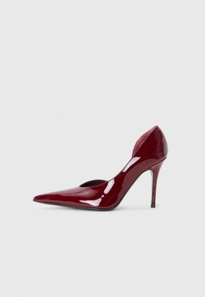 Red patent leather high-heeled pump with a pointed toe and cutout sides, featuring a sleek stiletto heel. Smooth, glossy finish.