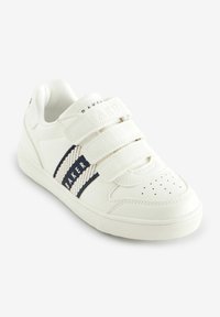 Zapatilla blanca con tres tiras de Velcro, que presenta una franja azul marino y la marca "BAKER". Textura de cuero suave con diseño de puntera perforada.
